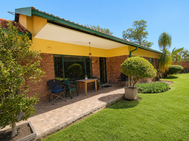 A covered patio area featuring tiled flooring and exposed brick walls, overlooking a well-maintained garden with established landscaping.