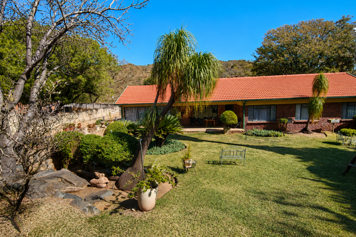 A spacious rear garden featuring a well-maintained lawn, mature landscaping, and a brick-built house with a classic terracotta tiled roof.