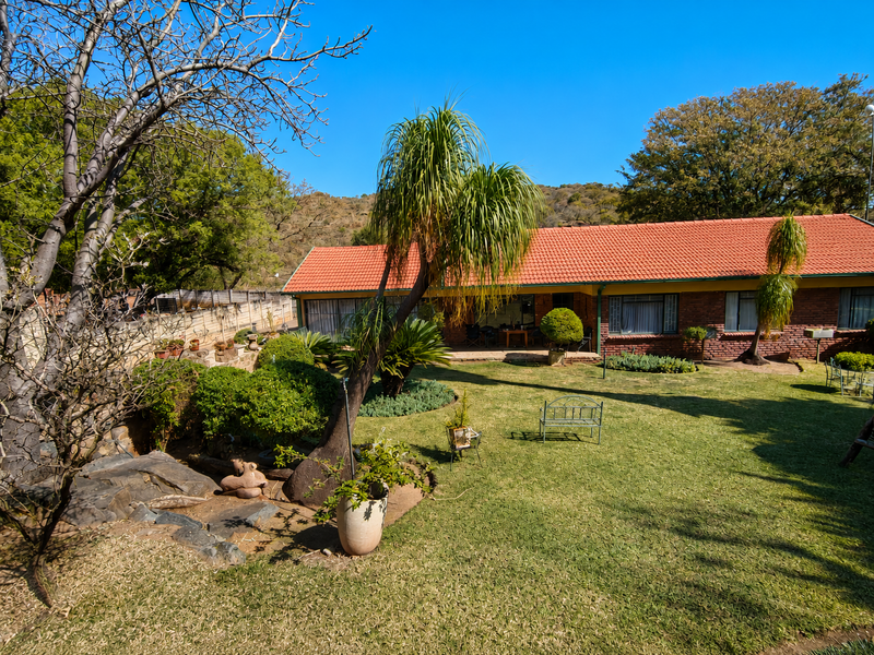 A spacious rear garden featuring a well-maintained lawn, mature landscaping, and a brick-built house with a classic terracotta tiled roof.