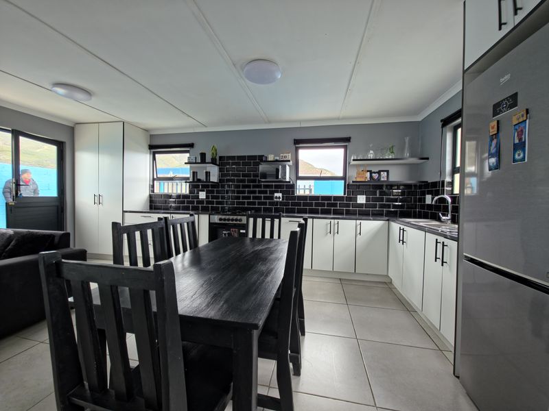 Modern open-plan kitchen featuring white cabinetry, black subway tile backsplash, tiled flooring, and integrated appliances, creating a clean and functional cooking and dining space.