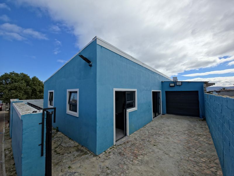 Rear exterior view of the property featuring a paved driveway, single garage, and blue painted facade with sliding door access.