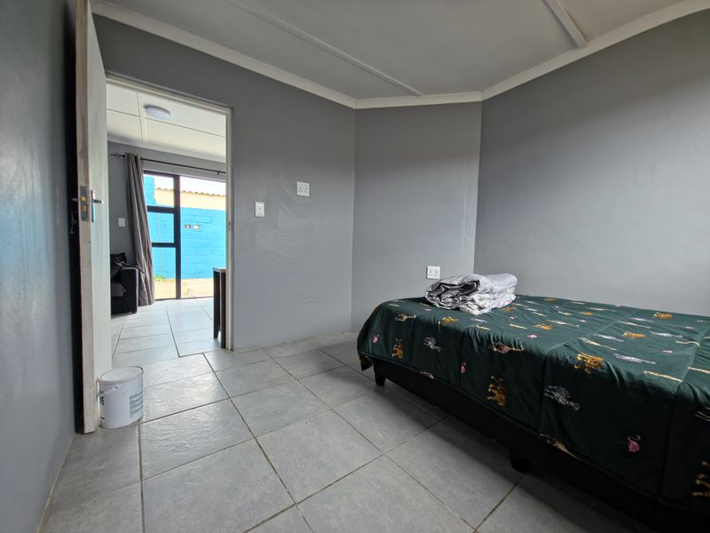 A simple bedroom featuring grey painted walls and tiled flooring, with a doorway leading to an adjacent living area.