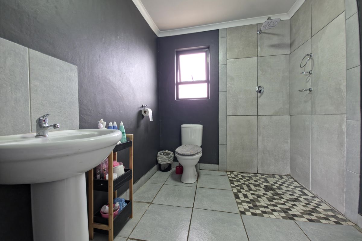A modern bathroom featuring a pedestal basin, a walk-in shower with tiled walls, and a toilet, finished with neutral floor tiles and dark accent walls.