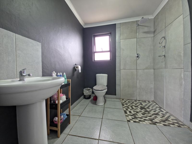 A modern bathroom featuring a pedestal basin, a walk-in shower with tiled walls, and a toilet, finished with neutral floor tiles and dark accent walls.
