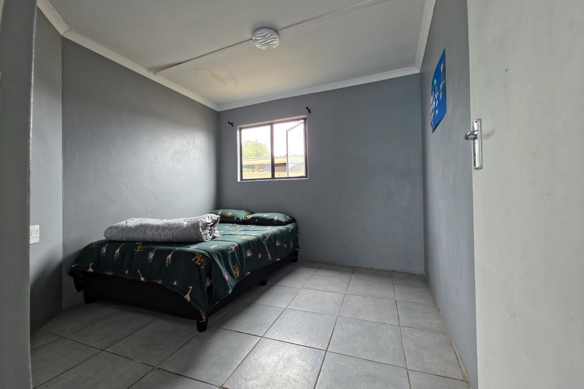 A bedroom featuring grey painted walls, tiled flooring, and a single window. The ceiling shows signs of water damage.