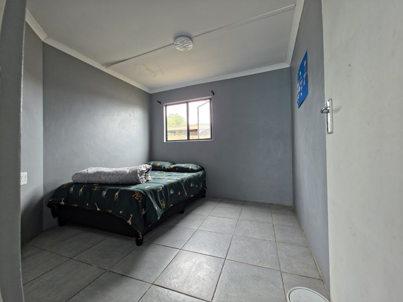 A bedroom featuring grey painted walls, tiled flooring, and a single window. The ceiling shows signs of water damage.