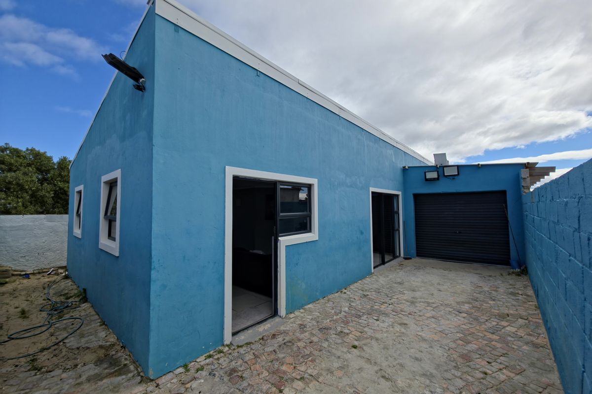 Rear exterior view of the property featuring a paved courtyard, roller garage door, and access via sliding glass doors.