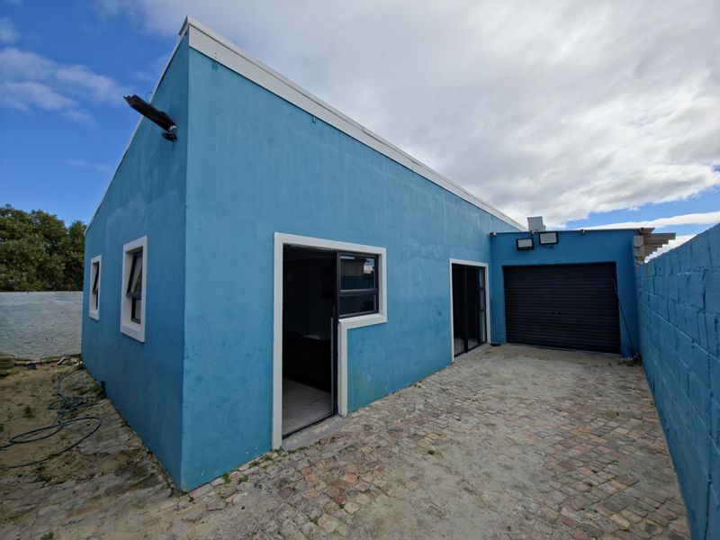 Rear exterior view of the property featuring a paved courtyard, roller garage door, and access via sliding glass doors.