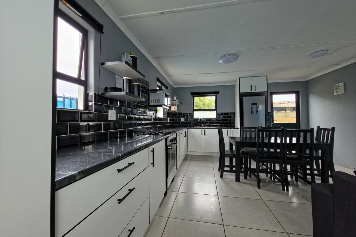 Modern kitchen featuring sleek white cabinetry, dark stone countertops, black subway tile backsplash, and integrated appliances with neutral floor tiling.