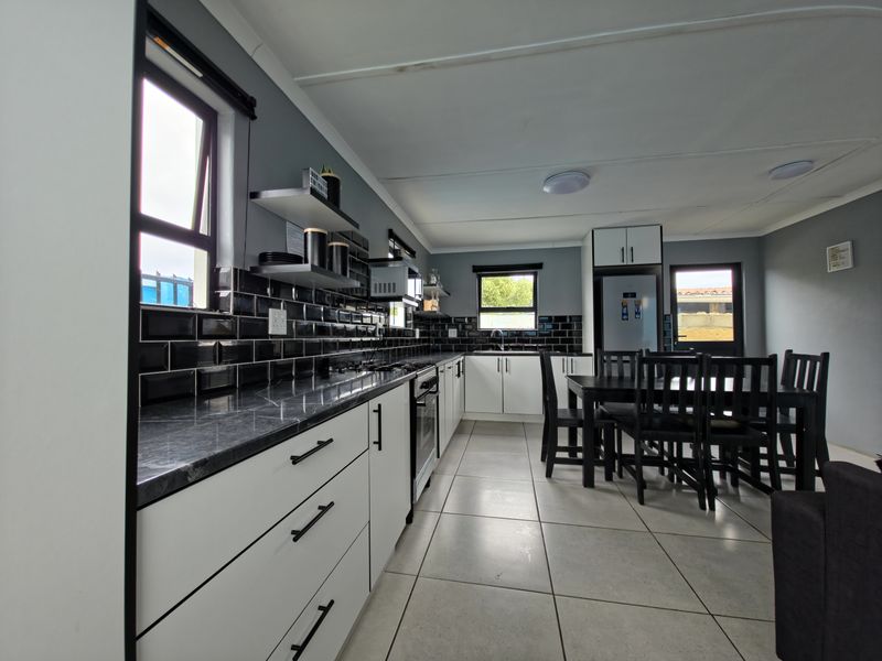 Modern kitchen featuring sleek white cabinetry, dark stone countertops, black subway tile backsplash, and integrated appliances with neutral floor tiling.