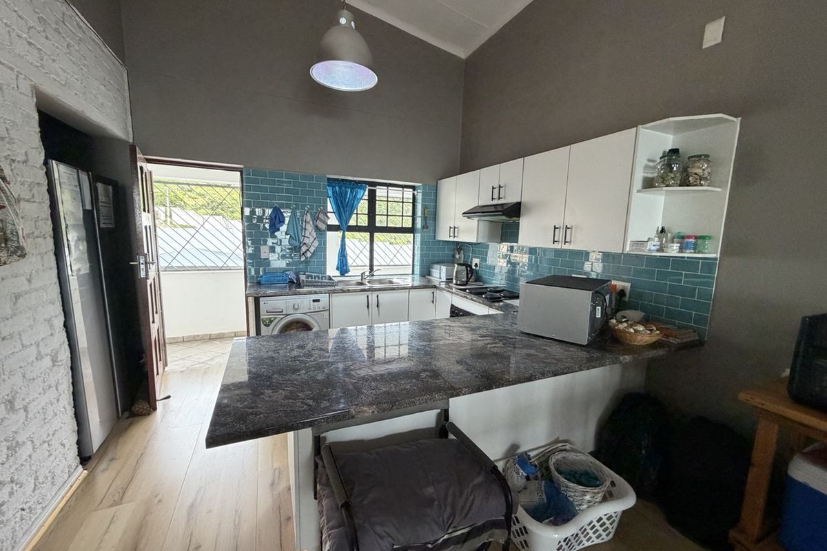 A functional kitchen featuring granite countertops, subway tile backsplash, white cabinetry, and an integrated hob with extractor fan, leading to an outdoor area.