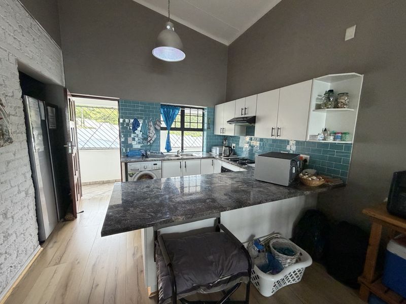A functional kitchen featuring granite countertops, subway tile backsplash, white cabinetry, and an integrated hob with extractor fan, leading to an outdoor area.