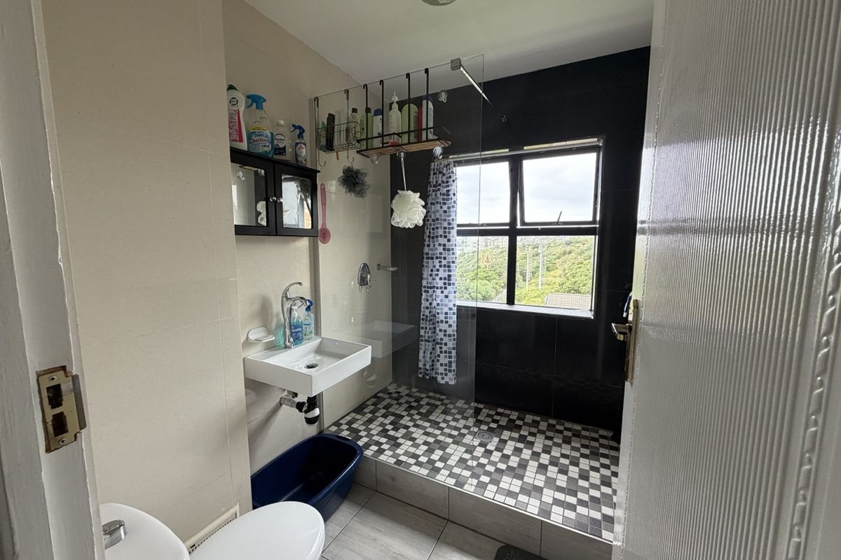 A functional bathroom featuring a walk-in shower with a glass screen, wall-mounted basin, and toilet, finished with contrasting wall and floor tiling.