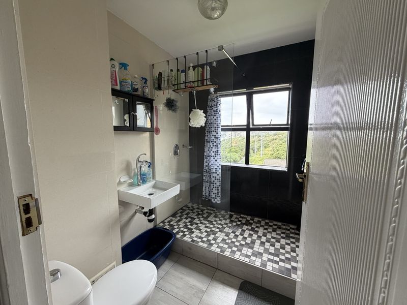 A functional bathroom featuring a walk-in shower with a glass screen, wall-mounted basin, and toilet, finished with contrasting wall and floor tiling.