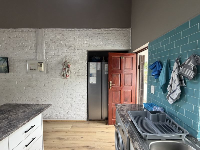 Kitchen area featuring exposed white brick walls, teal subway tile backsplash, laminate countertops, and wood-look flooring with direct access to an exterior door.