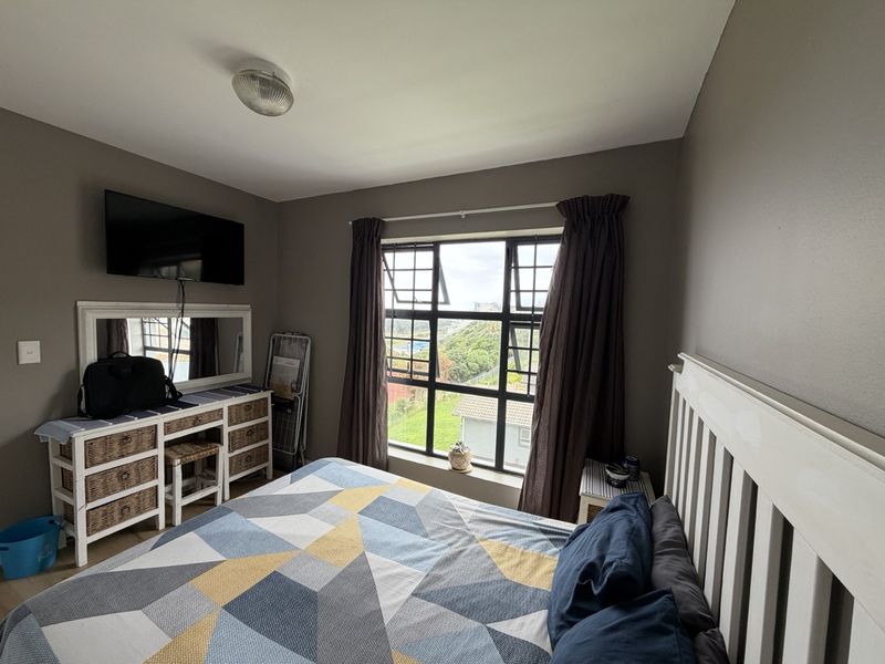 A bedroom featuring a large window with natural light, neutral wall tones, and a ceiling light fixture.