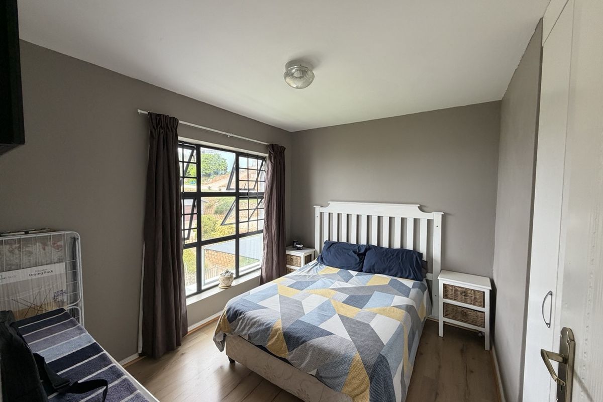 A functional bedroom featuring laminate flooring, a built-in wardrobe, and a large steel-framed window providing natural light.