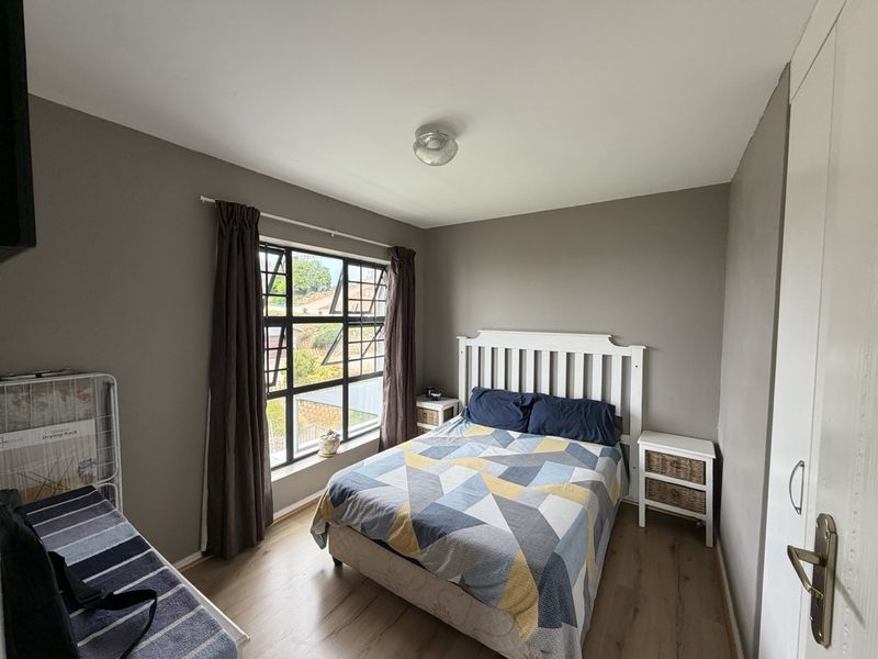 A functional bedroom featuring laminate flooring, a built-in wardrobe, and a large steel-framed window providing natural light.