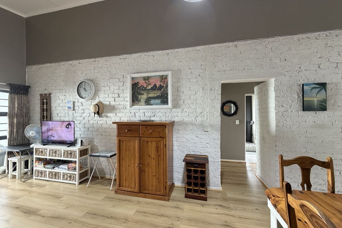 Living area featuring a characterful white-painted exposed brick wall and modern laminate flooring, providing a bright and textured backdrop for the space.