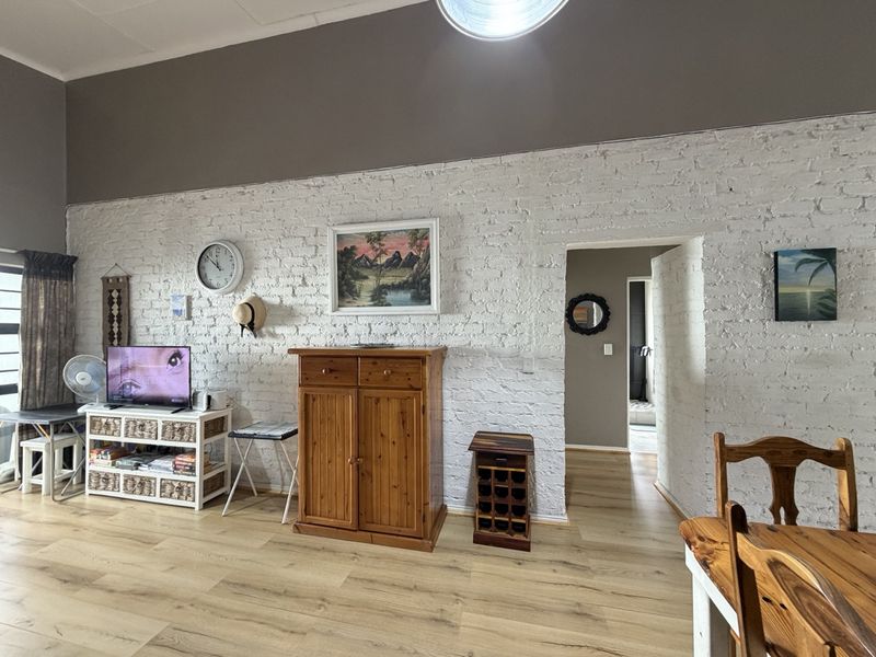Living area featuring a characterful white-painted exposed brick wall and modern laminate flooring, providing a bright and textured backdrop for the space.