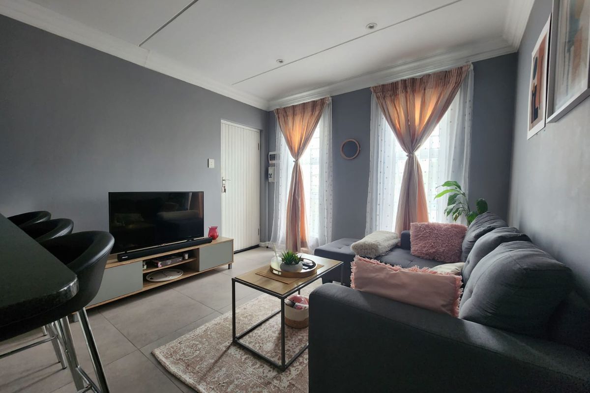 A well-maintained open-plan living area featuring neutral grey walls, large windows with natural light, and modern tiled flooring.