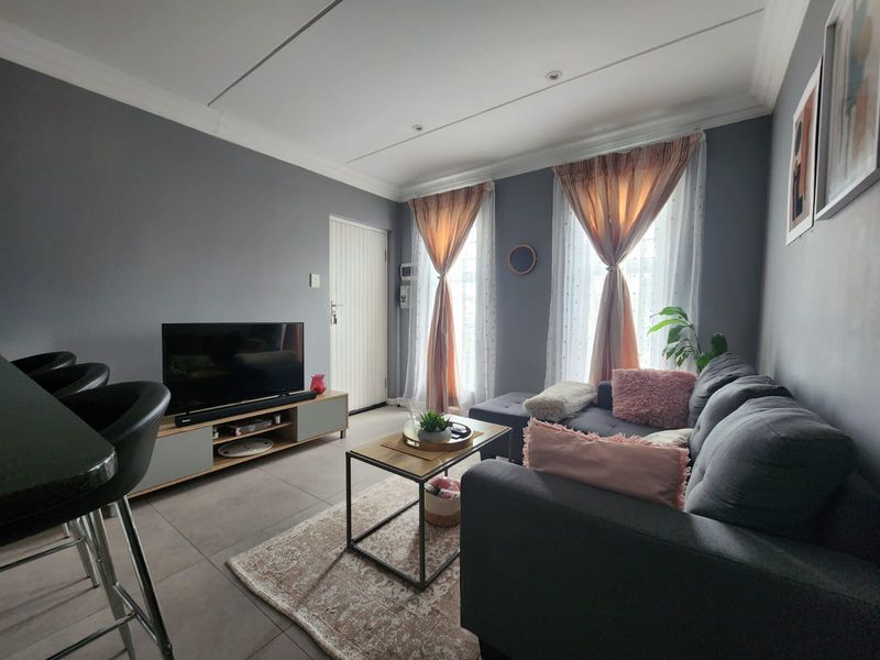 A well-maintained open-plan living area featuring neutral grey walls, large windows with natural light, and modern tiled flooring.