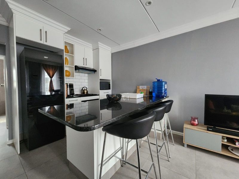 Modern open-plan kitchen featuring a granite island, white cabinetry, subway tile backsplash, and integrated appliances, seamlessly flowing into the living area.