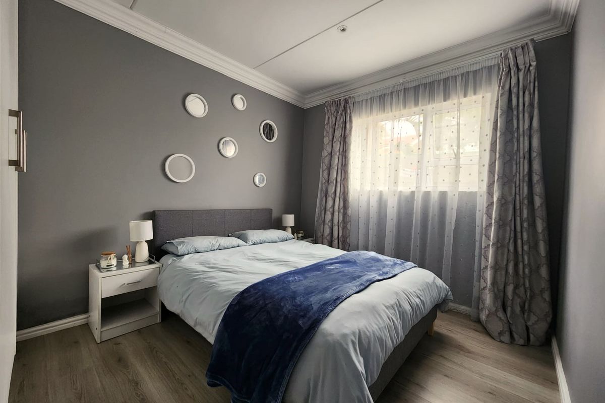 A well-maintained bedroom featuring laminate flooring, crown molding, and a window with curtains.