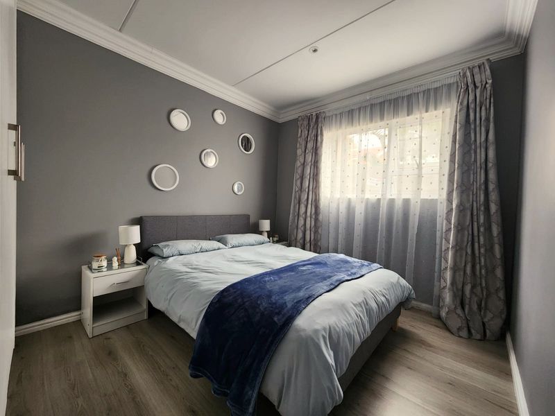 A well-maintained bedroom featuring laminate flooring, crown molding, and a window with curtains.