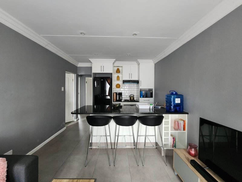 Open-plan kitchen and living area featuring modern white cabinetry, a black granite breakfast bar, subway tile backsplash, and neutral tiled flooring.