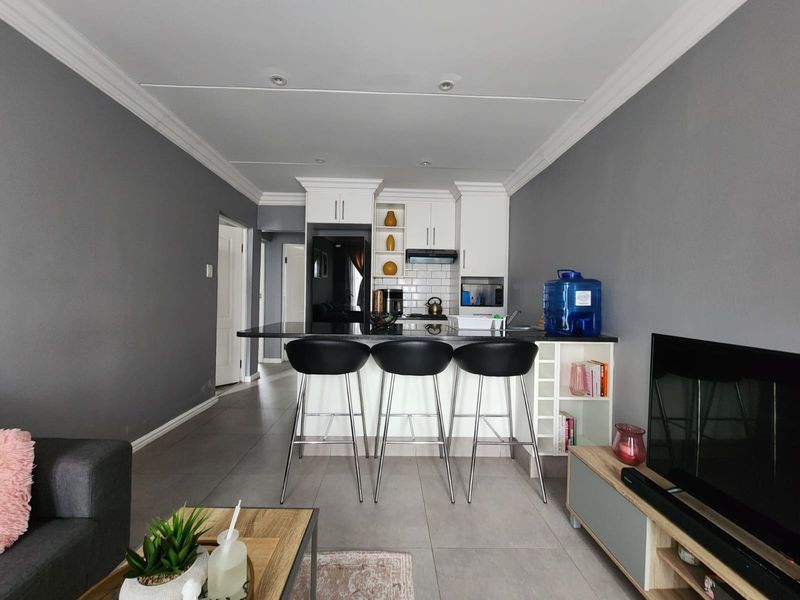 Modern open-plan living area featuring a sleek kitchen with white cabinetry, granite countertops, subway tile backsplash, and recessed lighting, seamlessly flowing into the living space.