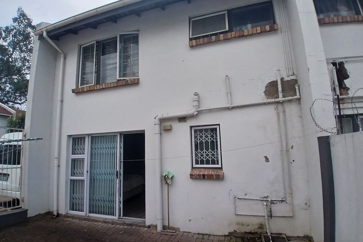 Rear exterior view of the townhouse featuring brick paving, sliding door access, and visible exterior plumbing and wall finish deterioration.