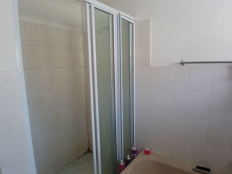 A functional bathroom featuring a shower enclosure and a bathtub with tiled wall finishes, requiring cosmetic updates to modernize the space.