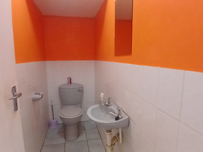 A compact bathroom featuring a toilet, wall-mounted basin, and tiled finishes, currently requiring cosmetic updates to improve its overall aesthetic appeal.