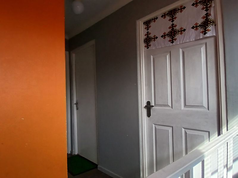 A hallway area featuring panelled interior doors and a staircase railing, showing signs of wear on the painted surfaces.