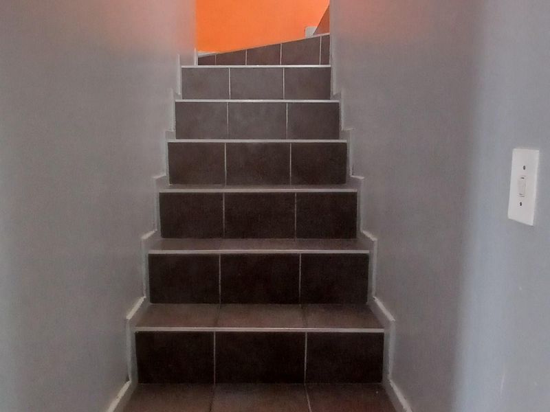 A staircase with dark tiled steps leading to an upper level, featuring grey and orange painted walls.