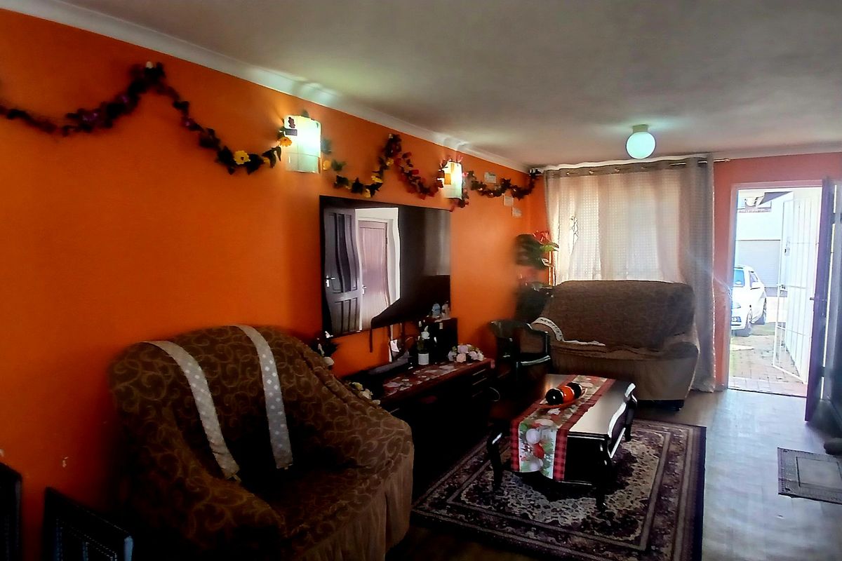 A living room area featuring orange walls, coving, and wall-mounted lighting, with direct access to the exterior.
