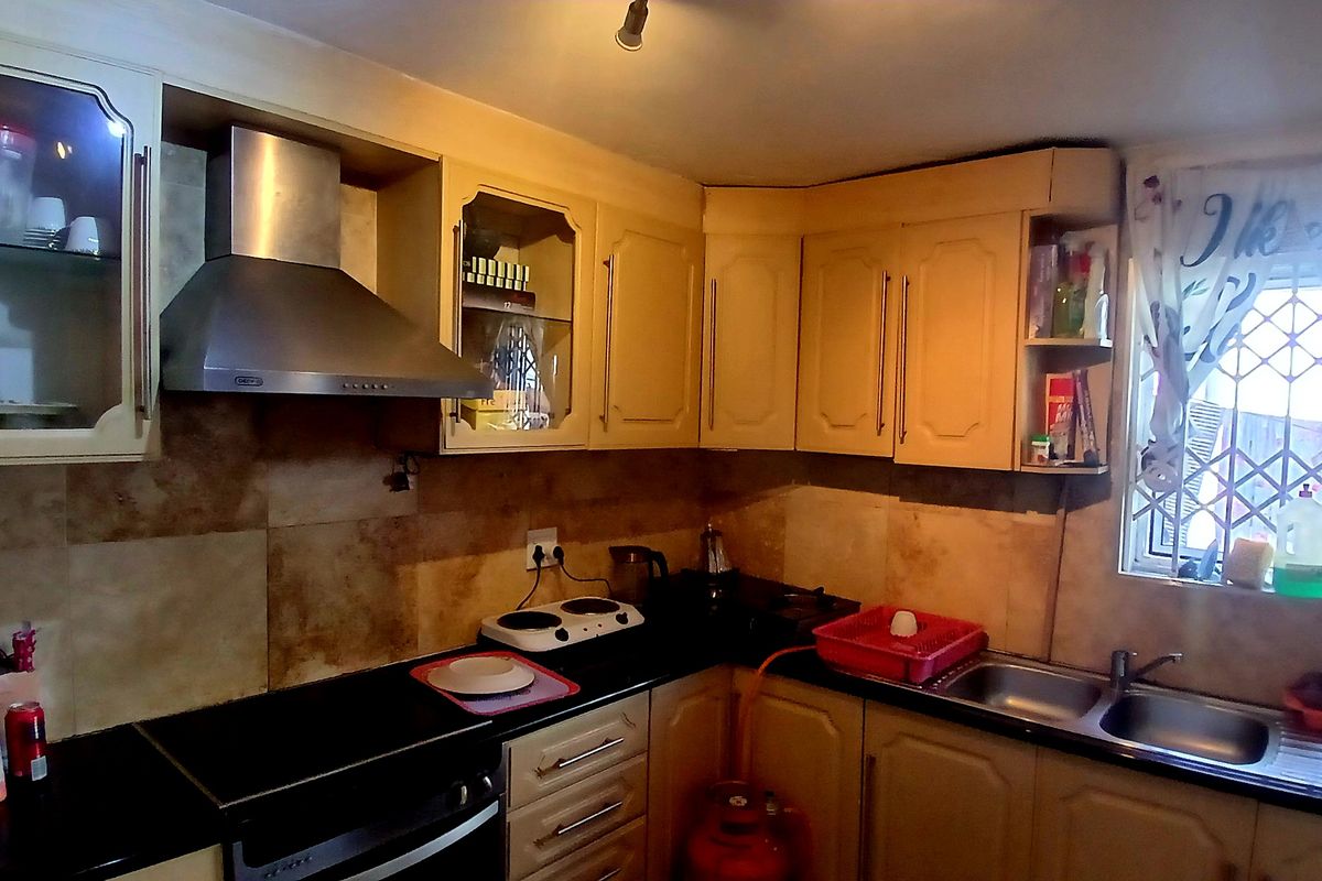 A functional kitchen featuring built-in cabinetry, a stainless steel extractor fan, double basin sink, and tiled backsplash with security bars on the window.