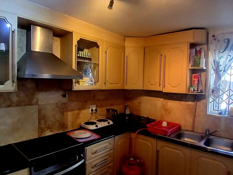 A functional kitchen featuring built-in cabinetry, a stainless steel extractor fan, double basin sink, and tiled backsplash with security bars on the window.