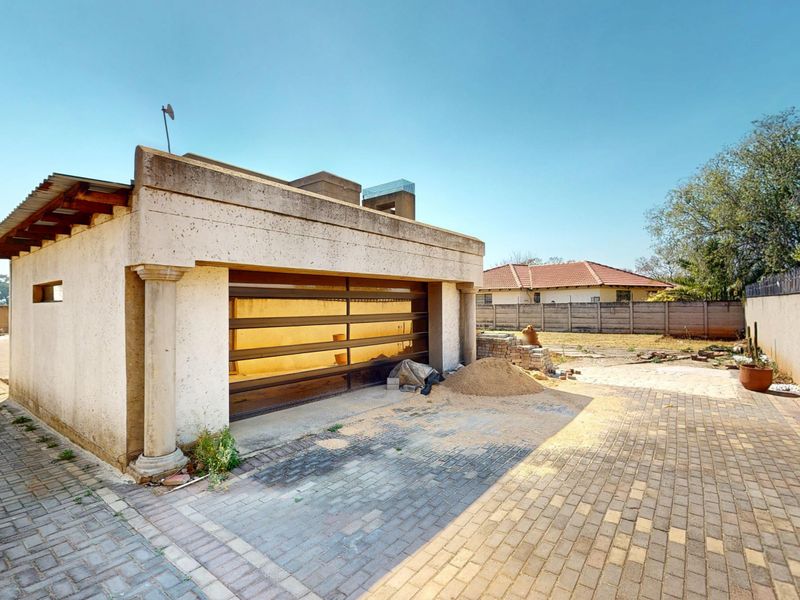 A detached garage structure featuring a modern garage door, set within a paved yard area with perimeter boundary walls.