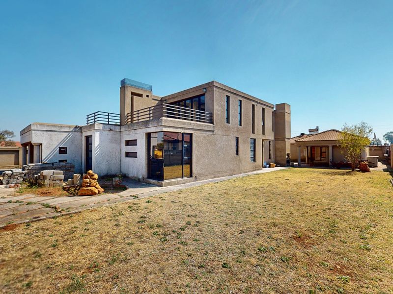 Rear view of a multi-level modern house featuring a balcony, large windows, and a spacious backyard with boundary walls.