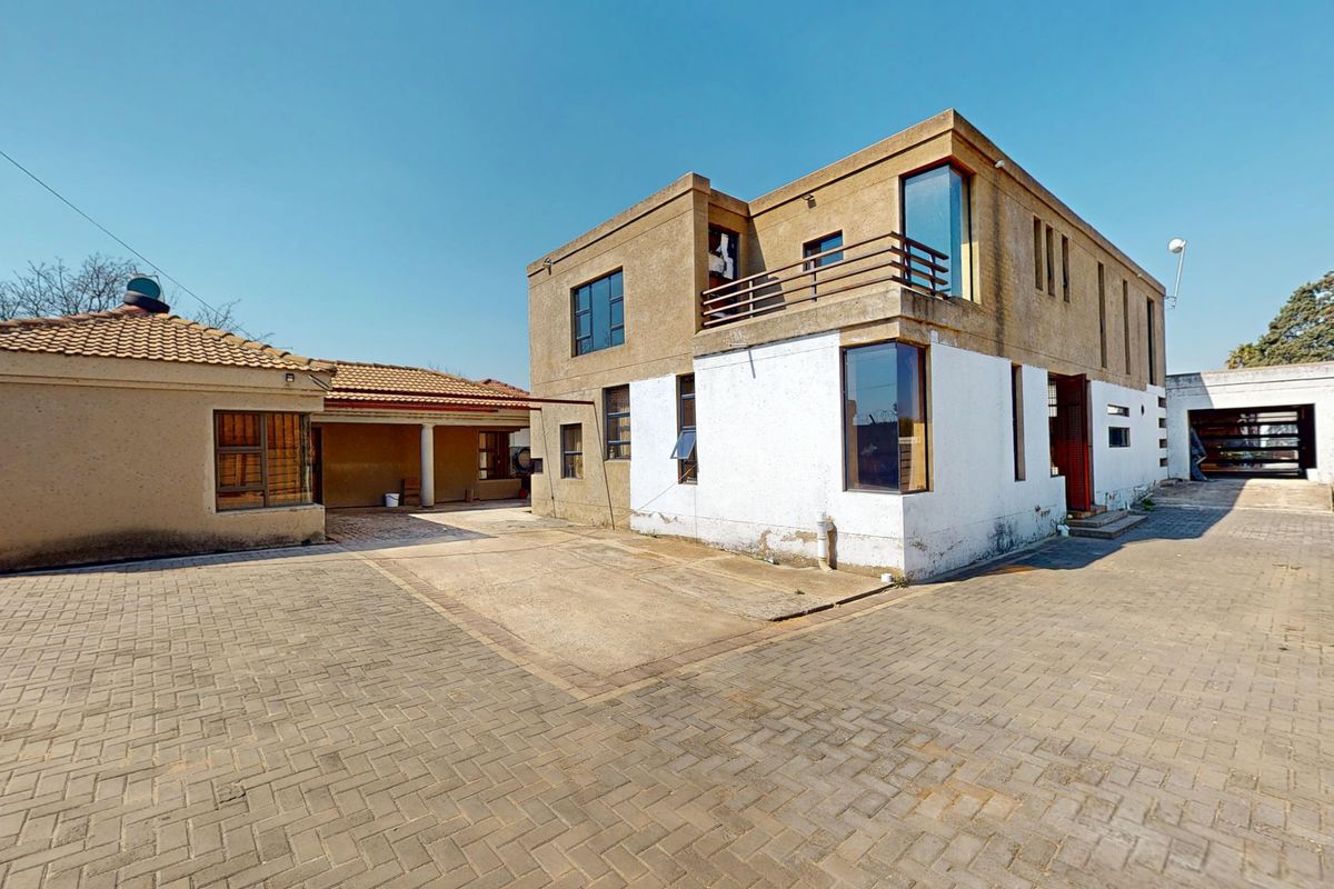 Rear view of a multi-story residential property featuring a paved courtyard, balcony, and a mix of textured and painted exterior finishes.