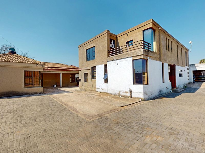 Rear view of a multi-story residential property featuring a paved courtyard, balcony, and a mix of textured and painted exterior finishes.