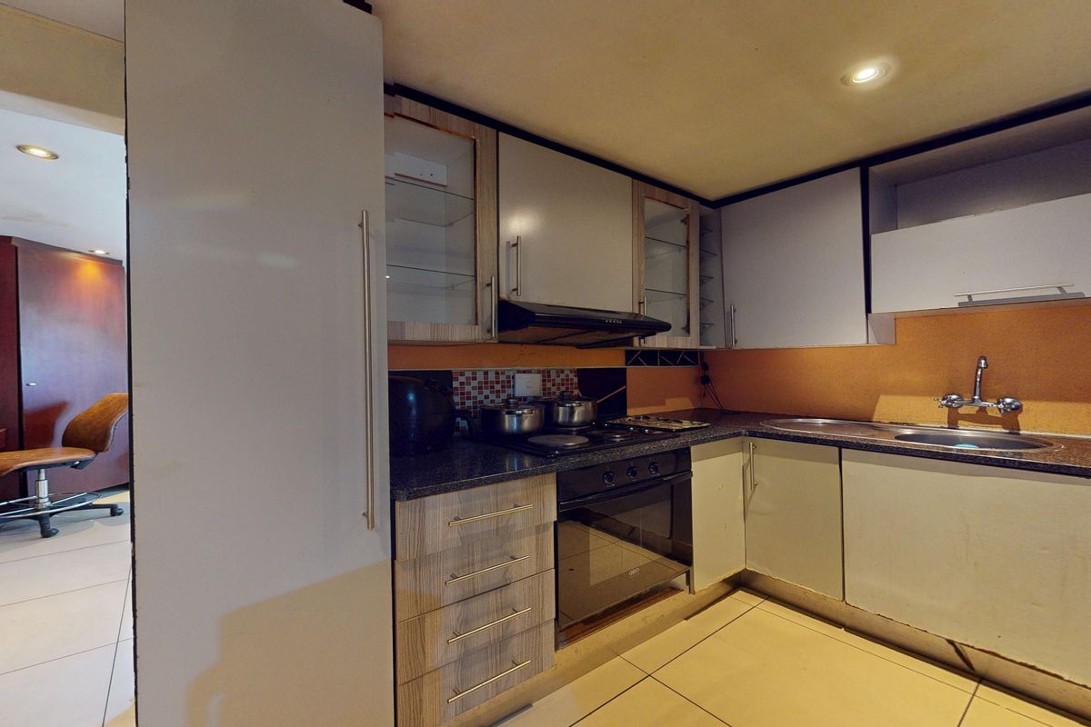 Compact kitchen featuring built-in cabinetry, integrated oven and hob, and tiled flooring, with adjacent access to a secondary living or office space.