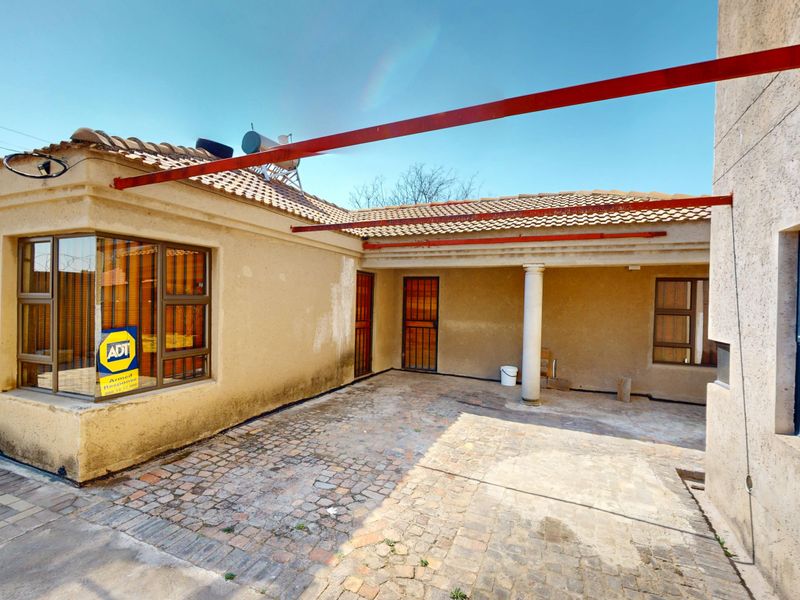 Rear exterior view of the house featuring a covered patio area, cobblestone paving, and a tiled roof with a solar water heater.