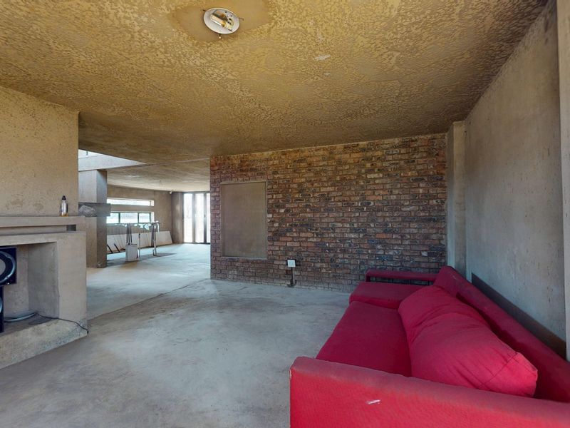 Spacious living area featuring exposed brickwork, concrete flooring, and a built-in fireplace, offering a blank canvas for renovation and modern interior design.