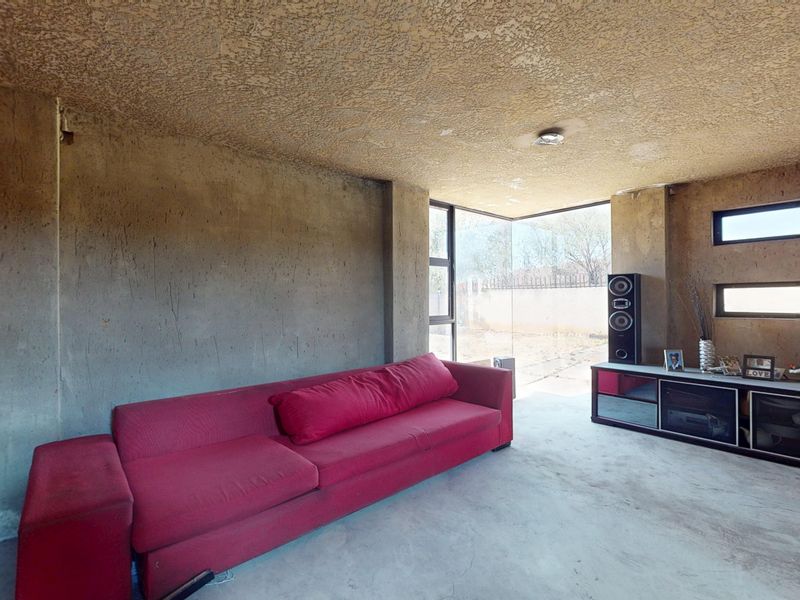 Living room featuring raw exposed concrete walls, textured ceiling, and concrete flooring with large corner windows providing natural light.