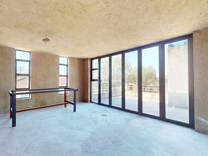 An unfinished living area featuring exposed concrete ceilings, brick walls, and large bi-fold doors leading to an outdoor space.