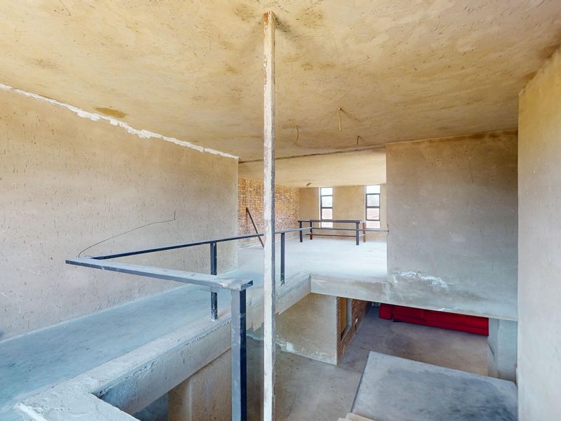 An expansive, unfinished open-plan interior space featuring raw concrete surfaces, exposed brickwork, and a metal balustrade, offering a blank canvas for renovation.