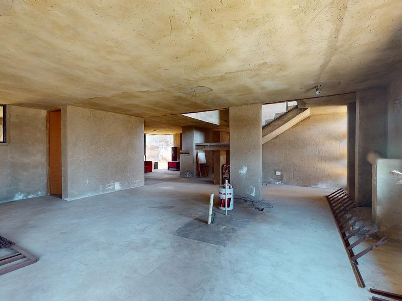 An expansive, unfinished open-plan interior space featuring raw concrete walls, flooring, and a staircase, offering a blank canvas for renovation and custom design.